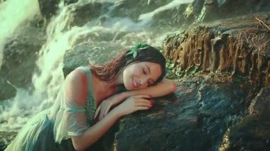 Islak su rengi elbiseli çekici bir kadın taşların üzerinde yatıyor. Narin, narin, narin, uyuyan bir nehir perisi tropik bir şelalenin yanında dinleniyor. Parlak güneşli bir gün. Hayalci kız..