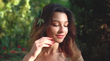 Yüzünde yumuşak bir gülümsemeyle saçlarını düzleştiren güzel bir esmer kadının portresi. Makyaj, parlak kırmızı manikür. Saçında sakulenty olan saç tokası. Yavaş Hareket Doğası