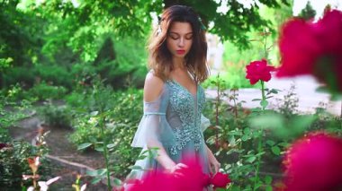 Sevgi ve şefkat ile çiçek açan bir güle dokunan genç bir kadının portresi. Lüks suluboya elbiseli bir kraliçe çiçek açan bir yaz bahçesinde yürüyor. Şık ve şık bir parti kıyafeti..