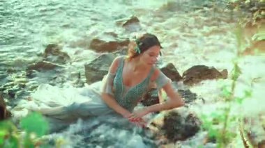Islak su rengi elbiseli çekici bir kadın taşların üzerinde yatıyor. Narin, narin, narin, uyuyan bir nehir perisi tropik bir şelalenin yanında dinleniyor. Parlak güneşli bir gün. Hayalci kız..