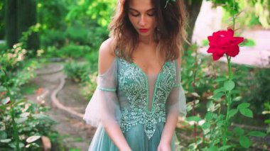 Çiçek açan bir güle dokunan bir kadının portresi. Eller ve çiçekler yakın plan. Kraliçe uzun suluboya elbiseler ve dantelli bir korse giyiyor. Peri masalı kızı. Hassas makyaj, ahududu dudaklar.