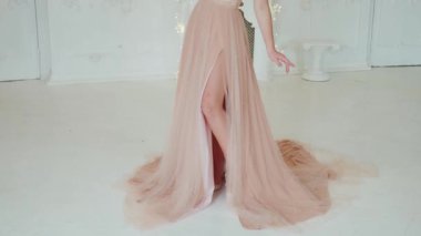 Mezun genç bir kızın portresi. Bej şeftali rengi, pembe, çıplak elbise, tren. Kadın sarı dalgalı saçlarına inci diyademine dokunuyor. Doğal makyaj malzemesi. Gülen surat. Beyaz perde arkası klasik klasik antika oda