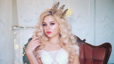 Sarışın prensesin portresini kapat. El sallayarak reddetme hareketi, yasağı reddetme. Kız hayır diyor. Kıvırcık saçlar. Altın taç. Kadın antika bir koltukta oturuyor. Doğal makyaj pembe dudaklar..