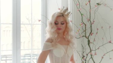 Genç, güzel, peri masalı prensesi modellik yapan bir portre. Beyaz perde arkası klasik oda içi Fransız penceresi. Kraliçe saç stili sarı dalgalı uzun saçlar. Ortaçağ kraliyet klasik lüks tacı.