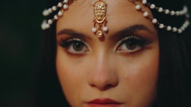 Güzel yüzlü, yakın plan kadın portresi. sahte uzun kirpikleri büyük kedi gözleri akşam makyajı, kameraya seksi bir bakış. Kahverengi gözler siyah saçlara bakarak açılır ve kapanır. Fantezi Elf peri kız tacı 4k.