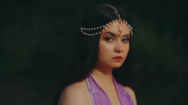 Fantezi peri kadının portresi. Uzun siyah saçlar üzerinde inci taç. Büyük kedi gözleri kırmızı dudaklar akşam makyajı, kameraya seksi güçlü bir bakış. Elf kız tanrıçası. Gizemli gece ormanı