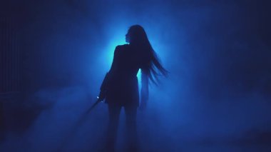 Gürültülü video. Karanlık fantezi sanat silueti kadın asker. Kız başını sallıyor, uzun dalgalı saçlar rüzgârda uçuşuyor. Savaşçı kraliçe eski iki kılıcı elinde tutuyor. Siyah arka plan yeşil ışık dumanı