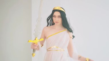 Fantezi kadın portresi Kraliçe savaşçı elinde kadim çelik kılıç tutuyor. Yaratıcı tasarım ipek elbiseler beyaz şık elbise altın kaplama klasik kostüm. Uzun esmer saçlı. Model güzellik yüzü.