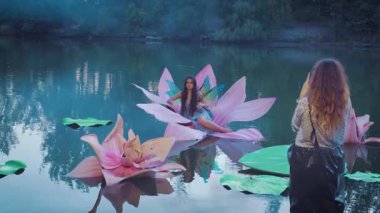 Çekim sürecinin sahne arkasında çekim yapan kadın fotoğrafçı, Thumbelina 'nın su görüntüsüyle poz veren bir fotoğrafçı kız mankeni, açık hava yaratıcı fotoğraf çekimi yaz doğası, yaratıcı manzara büyük zambak 