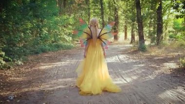 Siluet mutlu fantezi kadın orman perisi dikiz aynası. Kız elf prensesi toprak yolda yürümekten zevk alıyor. Sarı kostümlü kelebek kanatları. Yeşil yapraklar, yaz doğası..