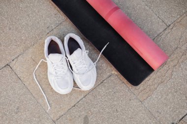 Açık havada beyaz spor ayakkabıları ve pembe spor paspası. 