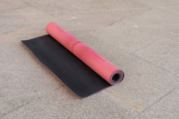 Rolled pink fitness mat on asphalt sidewalk on urban street, copy space, urban lifestyle 