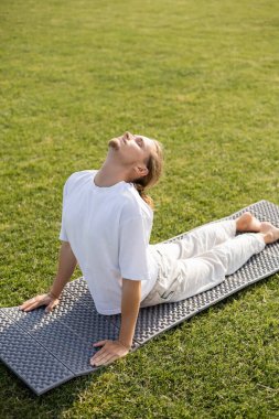 Gözleri kapalı genç sakallı adam kobra pozunda yoga minderinde meditasyon yapıyor. 