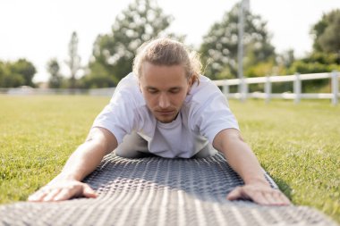 Yüzeyde meditasyon yapan genç adam gözleri kapalı yeşil çimenlikteki yoga minderinde.