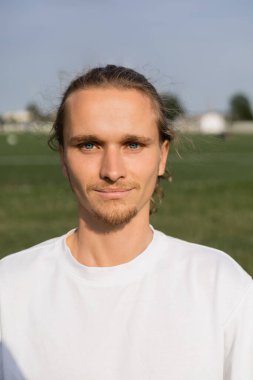 Dışarıdaki kameraya gülümseyen beyaz tişörtlü genç sakallı yoga adamı portresi.