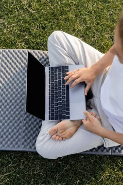 Çimenli çimlerde rahat yoga pozu verirken dizüstü bilgisayar kullanan biçilmiş adamın en iyi görüntüsü.