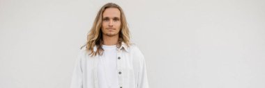 Keten gömlekli genç, uzun saçlı yoga adamı portresi beyaz duvarın yanındaki kameraya bakıyor, afiş.
