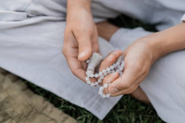 Açık havada meditasyon yaparken elinde boncuk tutan genç adam görüntüsü.