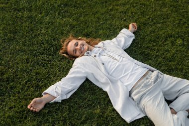 high angle view of overjoyed man in white shirt and pants relaxing on green grass outdoors