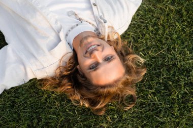 Genç ve mutlu bir adam, uzun sarı saçlı, çimenlerde dinlenirken kameraya bakıyor.