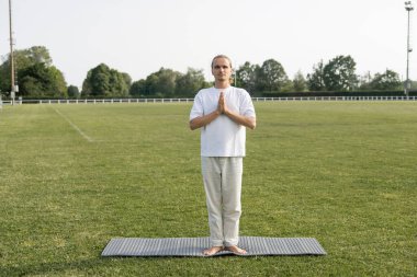 Çıplak ayaklı, keten pantolonlu, dağda meditasyon yapan yeşil çimenlikteki yoga minderinde dua eden bir adam.