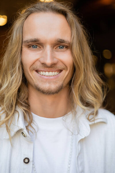 portrait of young and carefree yoga man with long fair hair looking at camera outdoors