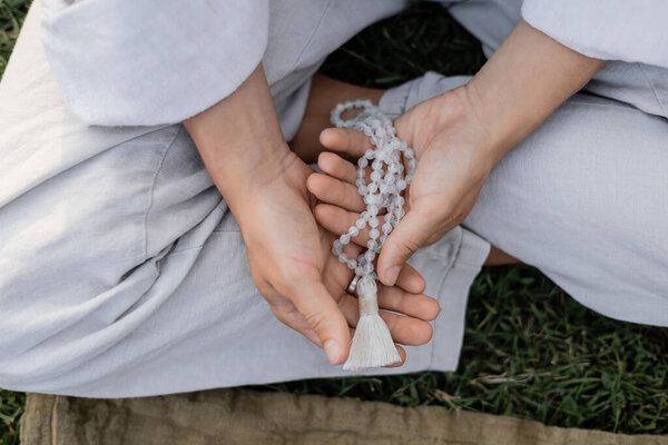 обрезанный вид человека йоги в льняной одежде, держащего бусины на открытом воздухе
