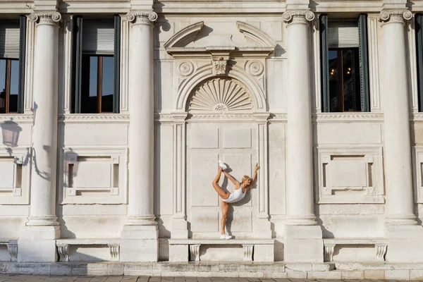 Vista laterale della sportiva in body e sneakers che si estende vicino all'edificio a Venezia — Foto stock