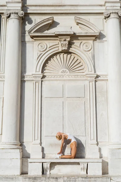Side view of blonde sportswoman in white sneakers and bodysuit stretching bodysuit on bench in Italy — Stock Photo