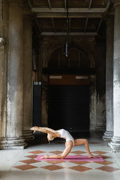 Sportiva in forma che pratica yoga su tappetino intorno a edifici antichi con colonne a Venezia — Foto stock