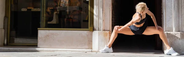 Mulher loira em tênis brancos, top de cultura preta e shorts que se estendem na rua urbana na Itália, banner — Fotografia de Stock