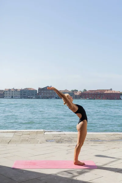 Бічний вид на біляву жінку в костюмі, що практикує йогу на набережній Венеції. — стокове фото