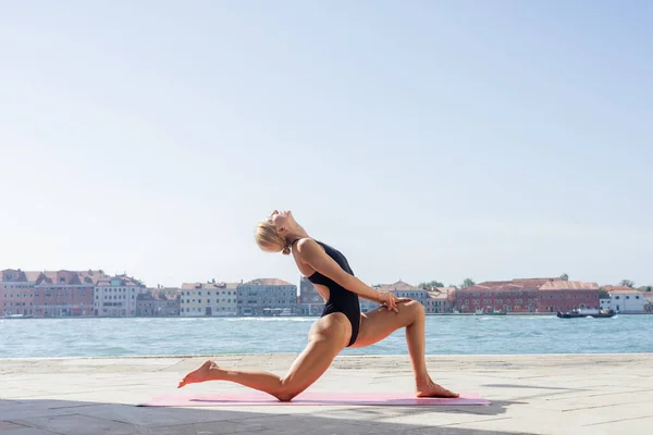Vista lateral de mujer en forma en body practicando yoga en la acera en Venecia - foto de stock