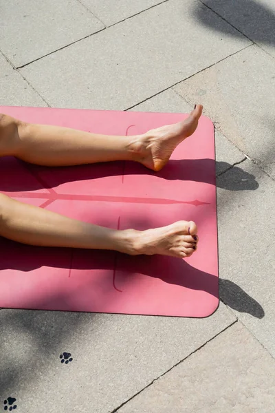 Ausgeschnittene Ansicht einer barfüßigen Frau, die sich bräunt und auf einer Yogamatte auf einer städtischen Straße liegt, Sommerkonzept — Stockfoto