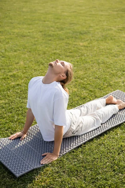 Jeune homme barbu avec les yeux fermés méditant en pose de cobra sur tapis de yoga — Photo de stock