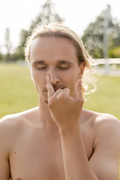 Uomo yoga senza maglietta con gli occhi chiusi tappando il naso durante l'esercizio pranayama all'aperto — Foto stock