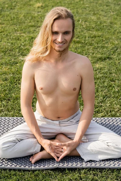 Überglücklicher hemdloser Mann mit langen Haaren praktiziert einfache Yoga-Pose auf grünem Rasen — Stockfoto