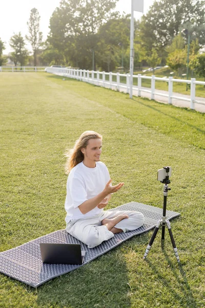 Jubelnder Yoga-Trainer zeigt mit Hand nahe Smartphone und Laptop auf Freiluftstadion — Stockfoto