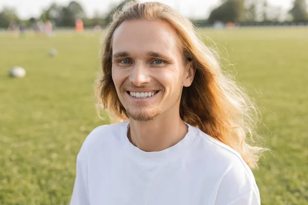 Portrait of overjoyed yoga man with long hair smiling at camera on blurred grassy field — Stock Photo