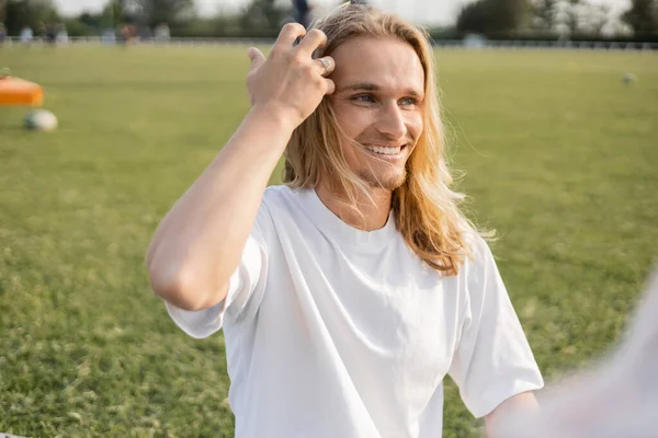 Jovem e despreocupado homem de ioga tocando cabelos longos e olhando para o exterior em primeiro plano borrado — Fotografia de Stock