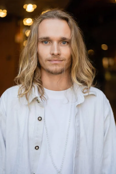 Portrait d'un homme de yoga aux cheveux blonds en chemise blanche regardant la caméra avec la ville floue sur le fond — Photo de stock