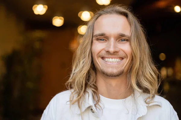 Retrato de homem de ioga de cabelos compridos overjoyed sorrindo para a câmera perto de luzes borradas ao ar livre — Fotografia de Stock