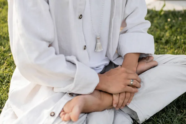Vue recadrée de l'homme en vêtements blancs assis dans la pose du lotus pendant la méditation à l'extérieur — Photo de stock