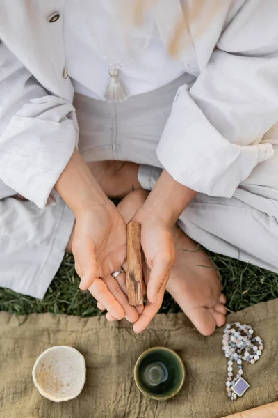 Vista superior do homem cortado em roupas brancas segurando palo santo vara perto de tapete de linho com copos de cerâmica e mala beads — Fotografia de Stock