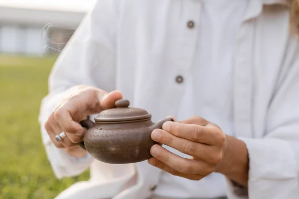Partial view of man in white cotton clothes holding oriental teapot outdoors — Stock Photo