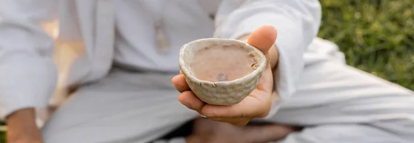 Cropped view of blurred man holding ceramic bowl with tea outdoors, banner — Stock Photo