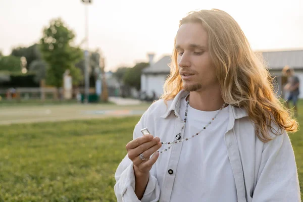 Pensoso uomo yoga in camicia di lino bianco guardando cristallo su perline mala mentre in piedi in campagna all'aperto — Foto stock