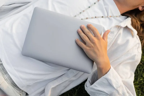 Vista dall'alto dell'uomo yoga ritagliato in vestiti bianchi e perline che tengono il computer portatile mentre si trova all'aperto — Foto stock