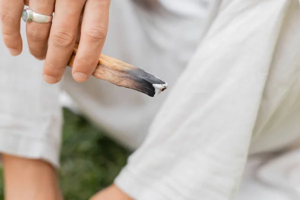 Частичный вид человека с серебряным кольцом на пальце, держащего тлеющий пало санто палка — стоковое фото