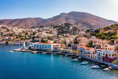 Symi (Simi) ada limanı, klasik gemi yatları, ada tepelerindeki evler, Ege Körfezi manzarası. Yunanistan adaları Rodos adasından tatil turları düzenliyor. Symi, Yunanistan, Dodecanese.